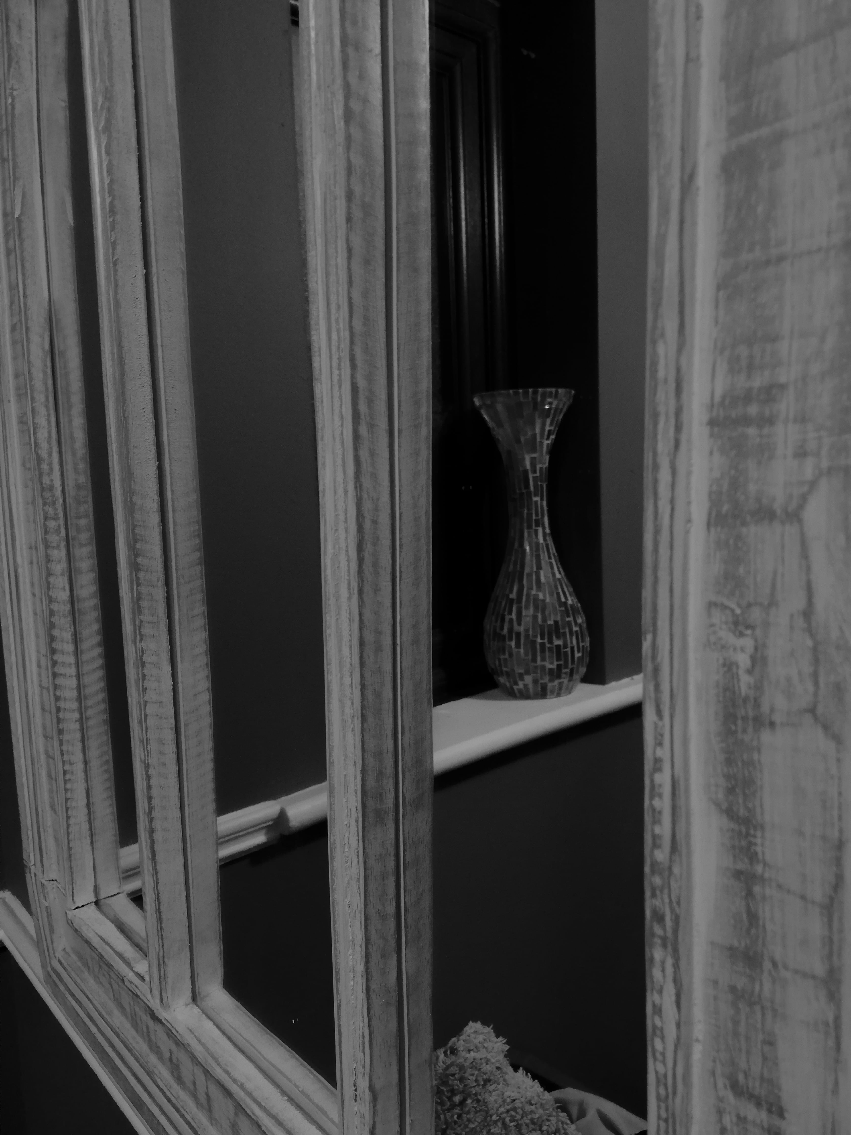 This is a black and white shot of a multicolored vase reflecting off of a wall mirror
